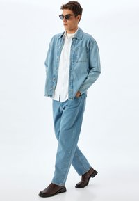 Giacca di jeans azzurro chiaro, camicia bianca e jeans azzurro chiaro; stivali marroni eleganti; occhiali da sole aggiungono contrasto; vestibilità rilassata e design con bottoni aperti.