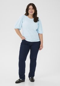 Light blue textured top with puff sleeves, featuring a diamond pattern; paired with dark blue jeans and black slip-on shoes.