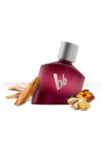 Botella de perfume de cristal morado oscuro con textura estriada y tapa plateada, acompañada de trozos de madera, raíz de jengibre y hierbas.