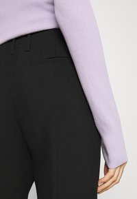 Černé tailored kalhoty s hladkou texturou a boční kapsou, kombinované s žebrovaným dlouhým rukávem lilového topu s přiléhavými manžetami.