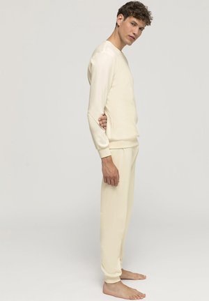 Conjunto de loungewear de color crema claro hecho de una tela suave; incluye una camiseta de manga larga con cuello redondo y pantalones de chándal a juego con puños elásticos.