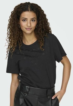 T-shirt nera in cotone con scollatura rotonda e dettagli floreali a intaglio sulla parte frontale, abbinato a pantaloni in pelle sintetica a vita alta.