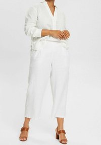 Löst sittande vit linneskjorta med en urklippt krage, parat med vita linnebyxor. Bruna klacksandaler med en spänndetalj.