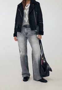 Zwarte suède jas met schapenvacht trim, grijze geruite trui, grijze flared jeans, zwarte instappers en een grote zwarte handtas.