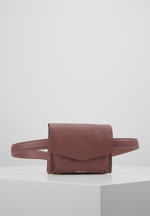 Sac banane en cuir marron avec rabat avant et couture blanche, présenté sur une surface blanche sur un fond uni gris clair.