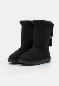 Bottines en cuir suédé noir avec une doublure en fourrure douce et texturée, dotées de nœuds décoratifs à l'arrière et d'une semelle extérieure robuste et texturée.