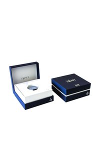 Deux boîtes bleues avec des lettres dorées. Une boîte est partiellement ouverte, révélant une montre dans un insert blanc. Designs lisses et élégants, couleurs contrastées.
