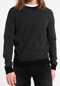 Maglione nero a maglia con motivo a pois bianchi, scollatura a girocollo, polsini e orlo a costine, silhouette attillata, tessuto testurizzato.