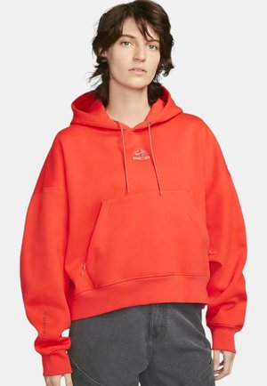 Rød oversized hoodie med en frontkangaroo-lomme, snørebånd og logopræget detalje. Blødt stof, cropped design og ribbede manchetter.