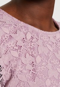 Ljuslila spetstyg med ett blommigt mönster med intrikata strukturer och urklippsdetaljer som skapar ett ömtåligt och luftigt utseende.