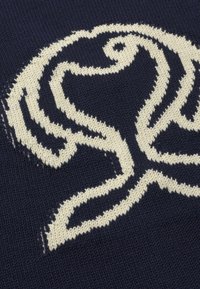 Motif abstrait d'oiseau en tricot blanc avec des lignes courbes sur un fond de tissu bleu marine foncé.