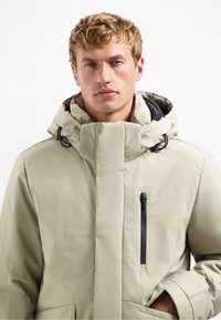 Beige geïsoleerde jas met een hoge kraag en een trekkoordcapuchon. Voorzien van een ritsborstzak en een elegante, gladde textuur.