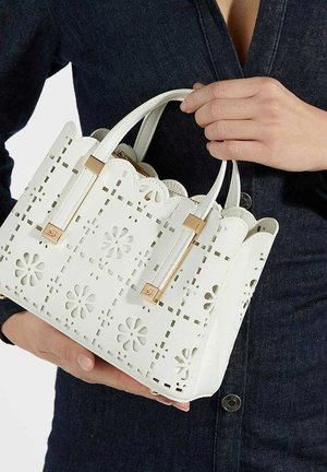 Witte handtas met golvende randen, bloemen uitsnijdingen, gouden hardware accenten en dubbele handvatten; gemaakt van gestructureerd materiaal.