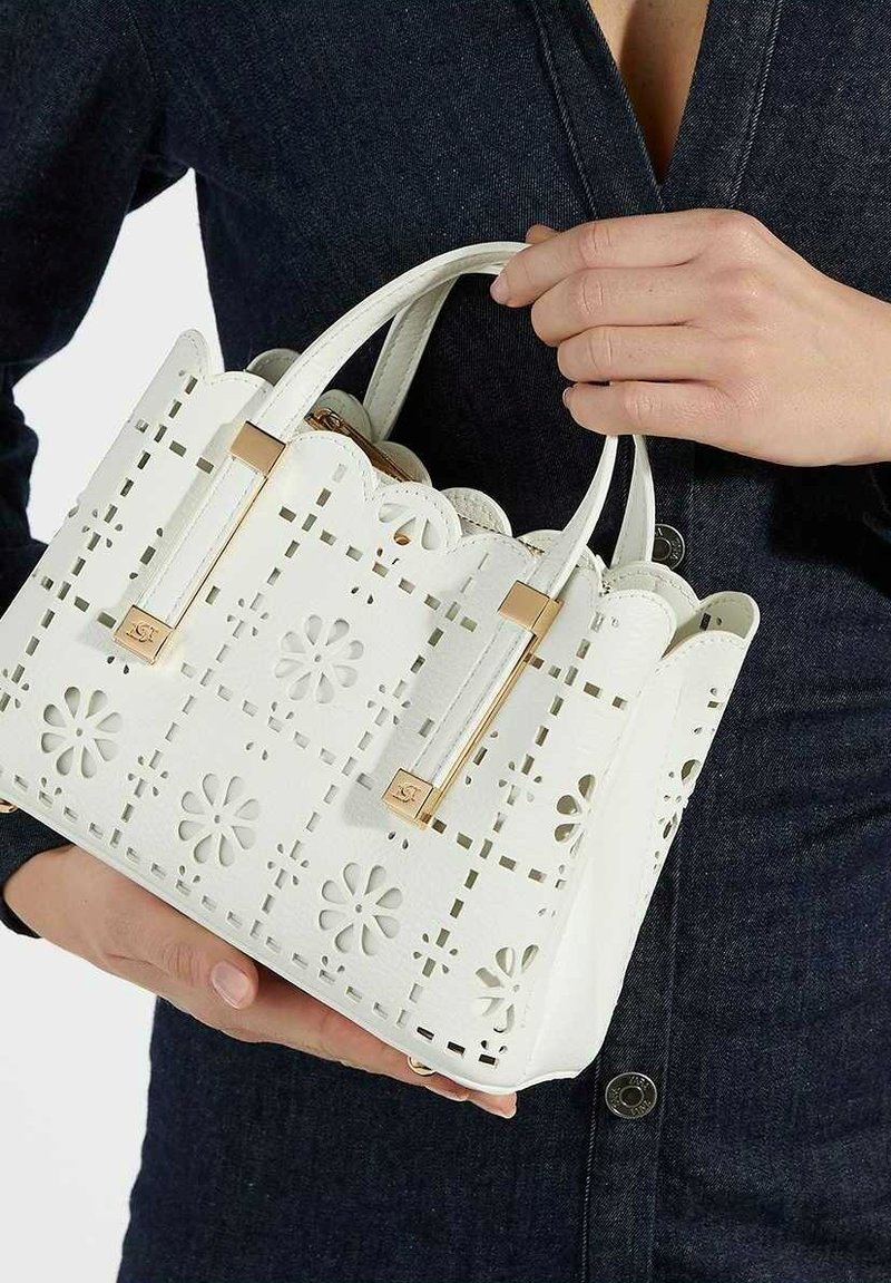 Weiße Handtasche mit gewellten Kanten, floralen Ausschnitten, goldenen Hardware-Akzenten und doppelten Griffen; aus strukturiertem Material gefertigt.