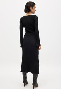 Abito a maglia nero a costine con maniche lunghe, schiena scoperta e orlo leggermente svasato, abbinato a stivali neri in pelle al ginocchio.