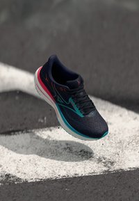 Navy running shoe with textured mesh upper, teal accents, and pink heel. Features a cushioned white sole and black laces.