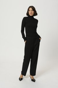 Pull à col roulé noir à manches longues, associé à un pantalon noir taille haute. Les accessoires comprennent des escarpins à bout pointu avec une petite boucle.