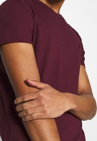 Burgunderfarbendes T-Shirt mit kurzen Ärmeln aus weichem Baumwollstoff, mit Rundhalsausschnitt und dezentem Logo auf der Brust.