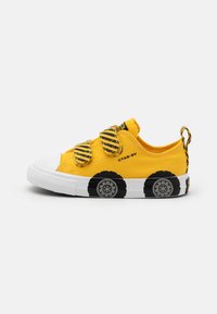 Gule lerrets-sneakers med svarte hjulgrafikker, borrelåsremmer, hvit gummi tå og såle, og en løkke på hælen for enkel bruk.