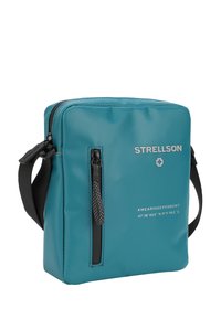 Teal syntetisk crossbody taske med en hovedrum lynlås, lynlås foran og hvid brandingtekst. Justerbar sort rem.