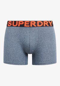 Blauwe gemêleerde katoenen boxershorts met een zwarte tailleband waarop de "SUPERDRY"-logo in oranje staat. Klassieke pasvorm met korte pijpen en platte naden.