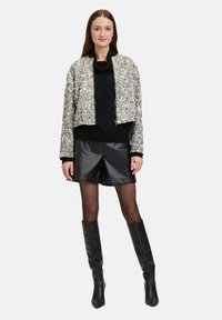Afgeknotte zilveren textuur jack, zwarte gebreide trui, zwarte leren shorts, knie hoge zwarte laarzen, gedragen door een model tegen een witte achtergrond.