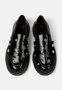 Zwarte schoenen met een glanzende leren afwerking, voorzien van brede banden en decoratieve zilveren knopen, van bovenaf weergegeven op een witte achtergrond.