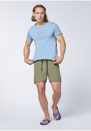 Helles blaues T-Shirt mit kurzen Ärmeln und rundem Druck, kombiniert mit olivgrünen Shorts und blauen Flip-Flops. Glattes Material und lässige Passform.