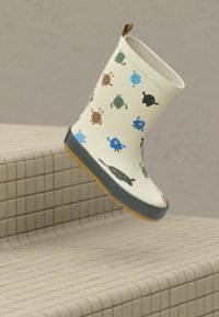 Botte de pluie crème avec des motifs de petits insectes colorés et une languette brune, placée au-dessus de marches carrelées beiges.