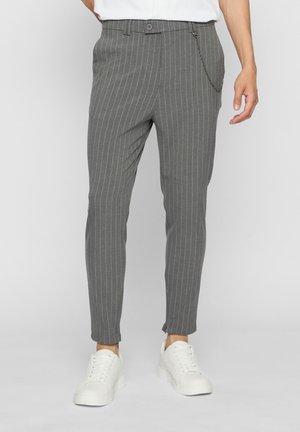 Hallid triibulised kitsad püksid külgmise ketti detailiga, kantud valgete tossude ja valge sissepandud särgiga.