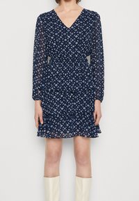 Námořnické modré šaty s dlouhými průhlednými rukávy, výstřihem do V, elastickým pasem a volánkovým lemem slušícím s bílým geometrickým potiskem po celém povrchu.