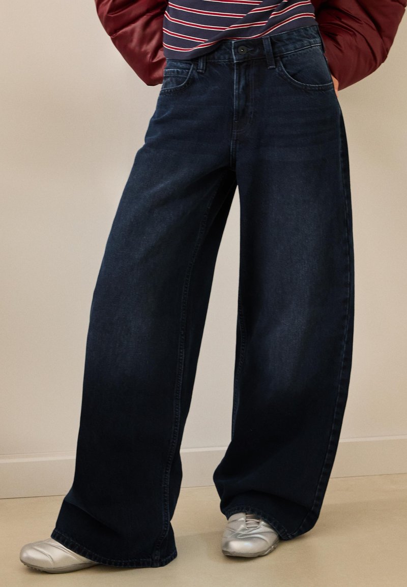 Széles szárú sötétkék farmernadrág magas derékkal, sima textúrával és finom, szabott részletekkel az első zsebeknél.