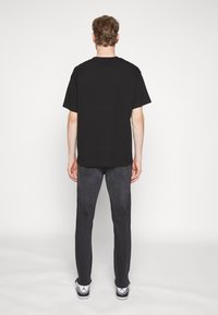 Camiseta de algodón negra de manga corta, combinada con jeans gris oscuro. El conjunto presenta un corte relajado y un diseño clásico.