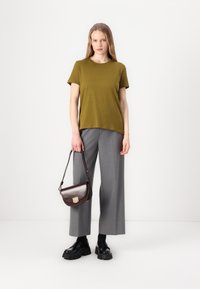 Olivgrön kortärmad t-shirt i kombination med grå vida byxor. En liten brun läderaxelväska med ett guldspänne. Svarta kraftiga skor.