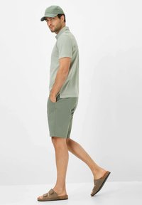 Lys grøn polo shirt, matchende shorts og brune sandaler. Casual design med en afslappet pasform. Iført en grøn kasket, stående i profil.