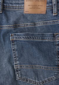 Granatowe dżinsy z ciemnego denimu z skórzaną metką w pasie i kontrastującymi pomarańczowymi przeszyciami. Posiadają detal tylnej kieszeni.