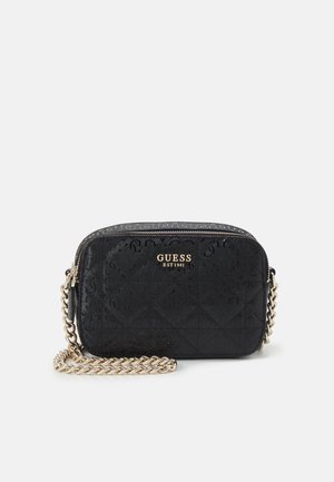 Schwarze gesteppte Umhängetasche mit goldener Kette und "GUESS EST 1981" Logo vorne vor weißem Hintergrund.