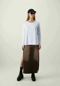 Top branco de manga longa combinado com uma saia maxi em degradê castanho com uma fenda lateral, usada com botas pretas de plataforma chunky e um boné preto.
