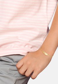 Tela a rayas rosa y blanca con un brillo sutil. Una pulsera dorada presenta un diseño curvado y un detalle de corazón con corte. También es visible tela gris.