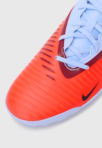 Nike fodboldsko med en lys orange syntetisk overdel med teksturerede riller, røde accenter, blå snørebånd og en fleksibel sål.