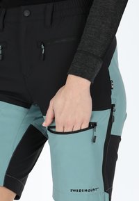 Shorts bicolore in nero e teal, realizzati in tessuto leggero. Presentano tasche con zip e una fascia elastica in vita per il comfort.