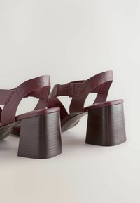 Burgundy leather sandals with wide straps and block heels. The heel features a ribbed texture, complementing the smooth upper design.