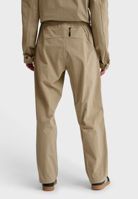 Beige vandtætte bukser med elastisk talje, baglomme med lynlås og en løs pasform. Lavet af letvægts, glat materiale.