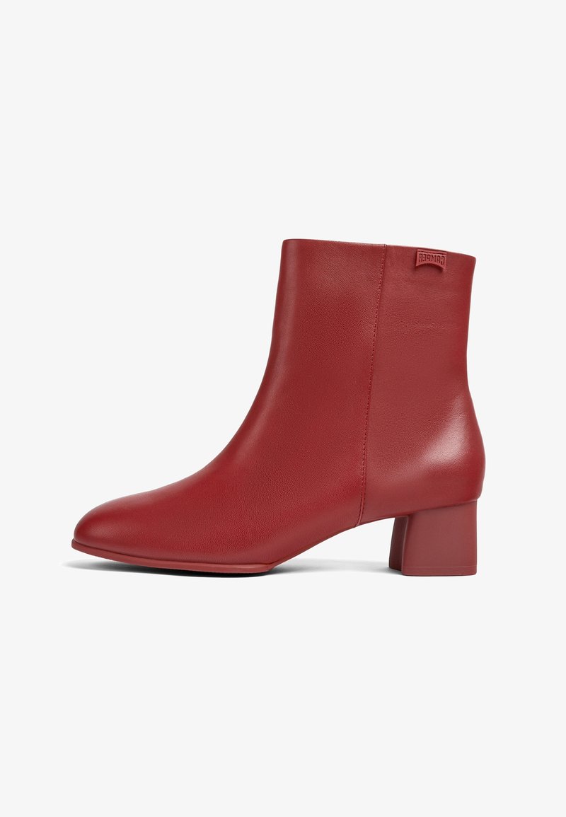 Botín de piel roja hasta el tobillo con tacón cuadrado y acabado suave, que presenta una pequeña etiqueta de marca cerca del borde superior en el lado exterior.
