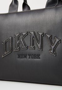 Zwarte leren tote bag met verhoogd "DKNY" logo en "NEW YORK" inscriptie, contrasterend met witte stiksels voor extra detail.