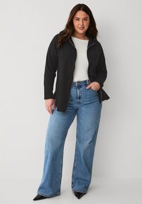 Sweat à zip noir avec capuche, associé à un jean large bleu clair. Les couleurs unies, le design décontracté et la texture douce du tissu sont des caractéristiques notables.
