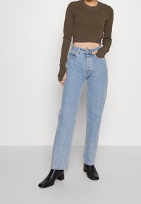 Oliivinvihreä lyhyt pitkähiha-paita yhdistettynä vaaleansinisiin korkeavyötäröisiin farkkuihin. Mallilla on mustat korolliset nilkkurit.