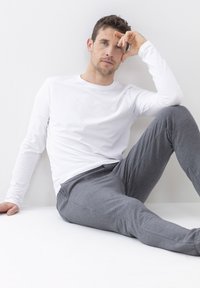 Witte lange mouw shirt gecombineerd met grijze joggingbroek. Het shirt heeft een ronde hals; de broek heeft een relaxte pasvorm en een zachte textuur.
