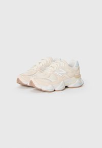 Une paire de baskets de sport en mesh et en suède beige et blanc avec de épaisses semelles blanches et des accents bleu clair, placées côte à côte.