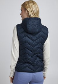 Gilet rembourré bleu marine avec capuche, doté d'un motif en chevrons, en matériau léger et à la coupe ajustée sur un pull léger.
